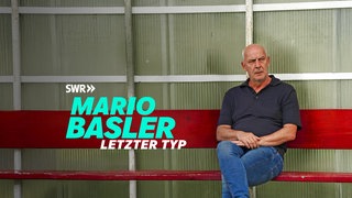 Mario Basler sitzt auf einer roten Bank am Spielfeldrand.