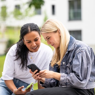 kolleginnen-schauen-auf-smartphone-draußen