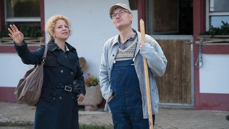 Bea und Karl vor dem Fallerhof, Bea macht eine ausschweifende Geste Richtung Himmel