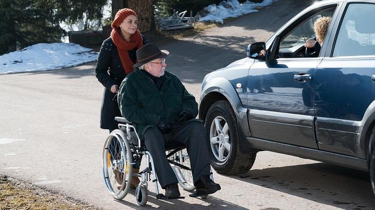 Jenny schiebt Hermann in seinem Rollstuhl, Bea sitzt in ihrem Wagen