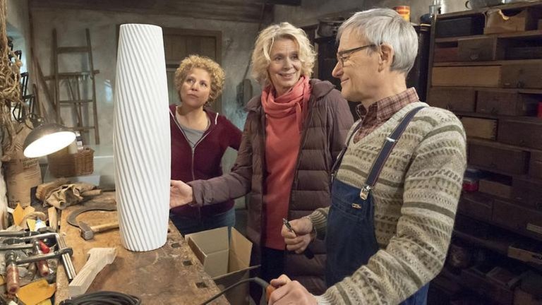 Kati zeigt Karl das Weihnachtsgeschenk für Johanna, im Hintergrund steht Bea