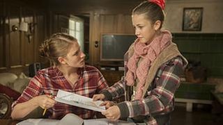 Lena steht bei ihrer Schwester Celine, die am Tisch sitzt und lernt