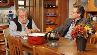 Hermann und Bernhard sitzen am Küchentisch und unterhalten sich in entspannter Haltung