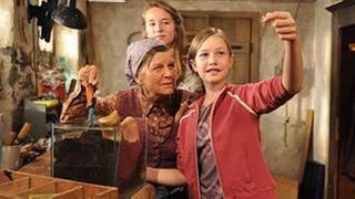 Annika und Lena stehen mit Lioba im Brunnengang, Lena hält ein Insekt hoch