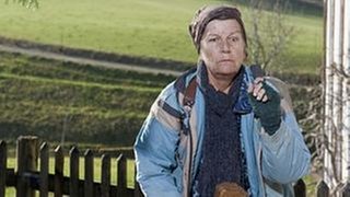 Lioba steht vor dem Fallerhof, in der Hand hält sie Wilhelms Stock