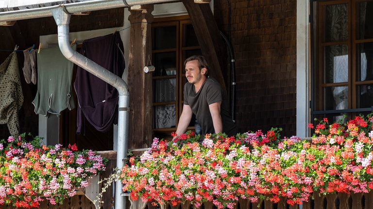 Sebastian (Dominik Stricker) auf dem Balkon des Fallerhofs an üppigen Geranien