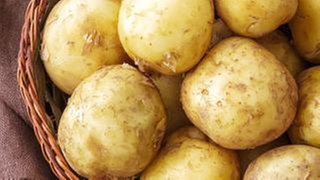 Pellkartoffeln mit Schale liegen in einem geflochtenen Korb auf einem Holztisch.
