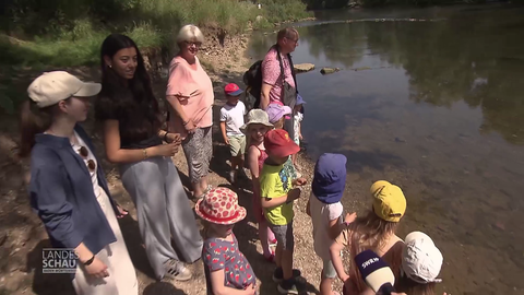Kinder stehen am Ufer und werfen eine Flaschenpost ins Wasser
