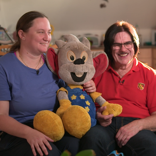 Sonja Schreiber und Ottmar Gamma sitzen zusammen auf einem Sofa. Zwischen ihnen eine große Euromaus, das Maskottchen des Europaparks. 