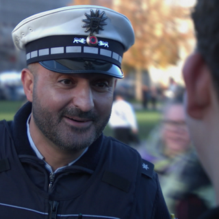 Luan steht in Polizeiuniform auf der Straße und spricht mit Passanten während seiner Präventionsstreife in Stuttgart.