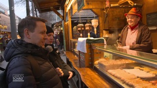 Zwei Lebensmittelkontrolleure stehen am Bratwurststand auf dem Mannheimer Weihnachtsmarkt