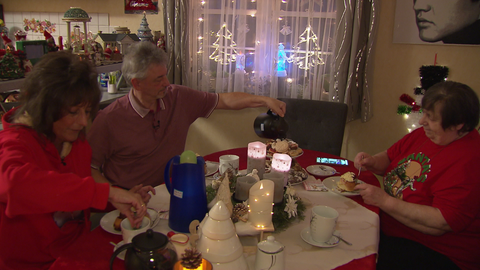 Zwei Frauen und ein Mann sitzen an einem weihnachtlich geschmückten Tisch und essen Zimtschnecken. 