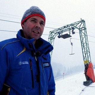 Matthias Schneider steht im Winter vor einem Skilift in Todtnauberg. Er trägt eine blaue Winterjacke und eine Mütze. Es liegt Schnee.