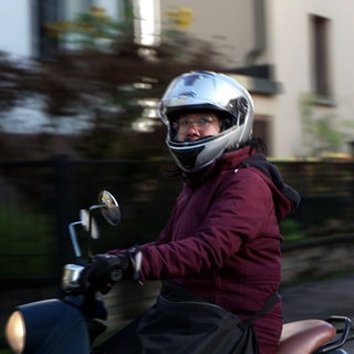Die Stuttgarter Pfarrerin Vinh An Vu fährt auf ihrer Vespa. Sie trägt einen Motorradhelm.
