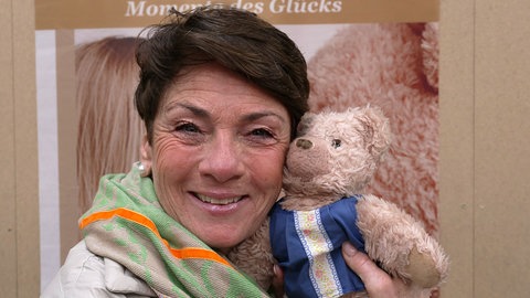 Sonja Faber-Schrecklein lächelt in die Kamera und hält ihren Kuscheltier-Bären an ihre Backe.