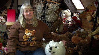 Claudia sitzt inmitten ihrer Teddybären. Sie trägt ein Teddybär-Shirt.