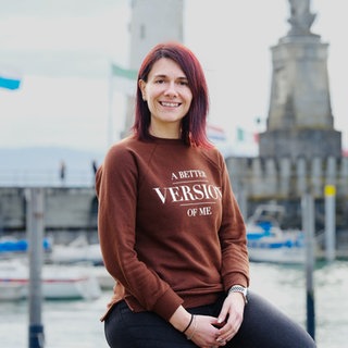 Aline Manglus sitzt vor dem Lindauer Leuchtturm und lächelt in die Kamera.