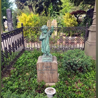Eine türkise Bronzestatue eines Engels steht auf einem Grabstein auf einem Friedhof.