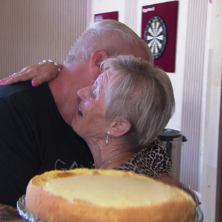 Erzieherin Gisela umarmt ein ehemaliges Kind, das sie betreut hat. In der anderen Hand hält sie einen Kuchen.
