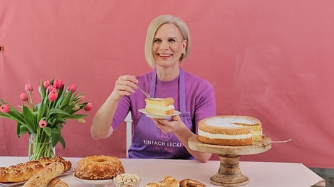 Stefanie Biedermann sitzt in ihrem Studio an einem Tisch. In der einen Hand hält sie einen Teller mit Kuchen und in der anderen ine Gabel.