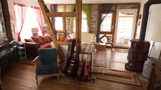 Die alte Mühle in Gundelsheim am Neckar von innen. Durch das Wohnzimmer gehen zwei Holzstreben, davor steht eine Reihe von Gitarrenkoffern. Rechts ist ein Kamin. Hinter den Holzstreben steht ein Sofa.