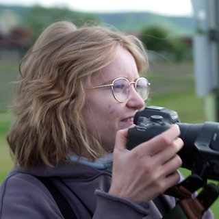 Birding - junge Frau mit Fotokamera in der Hand beim Beobachten von Vögeln