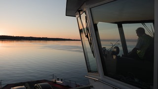 Eine Fähre steht auf dem Bodensee, auf der linken Seite sieht man den Sonnenaufgang.