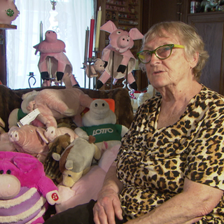 Seniorin sitzt neben ihrer Sammlung an Plüsch-Schweinen und Figuren.