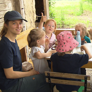 Kindergartengruppe sitzt an einem Tisch auf dem Hof von Bauer Heini