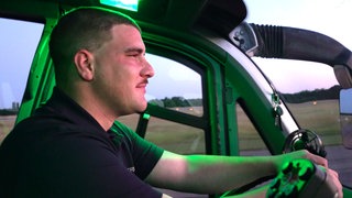 Lukas Weber sitzt in einem Feuerwehrwagen auf dem Gelände des Flughafens KarlsruheBaden-Baden und schaut in einen rötlichen Sonnenaufgang.