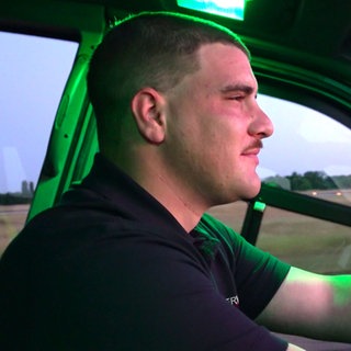 Lukas Weber sitzt in einem Feuerwehrwagen auf dem Gelände des Flughafens KarlsruheBaden-Baden und schaut in einen rötlichen Sonnenaufgang.