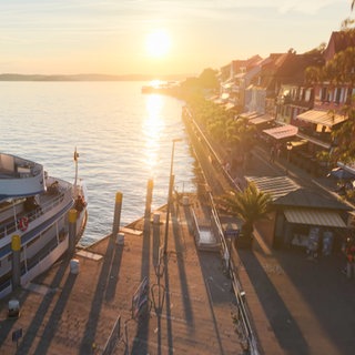 Die Seepromenade in Meersburg bei Sonnenuntergang. Links steht ein Schiff, rechts sind Häuser.