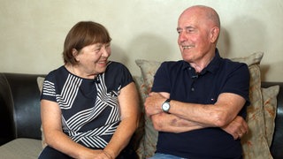 Uli und Gabi sitzen auf einem Sofa und lächeln sich an.
