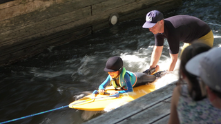 Ein Kind liegt auf einem Surfbrett und surft auf der "blackforestwave in Pforzheim".