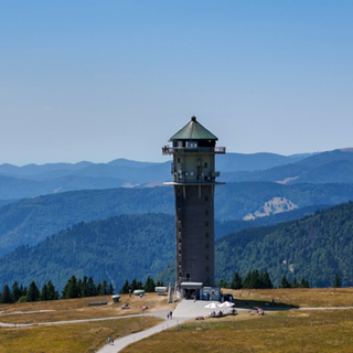 Der Feldbergturm im Sonnenschein. Im Hintergrund sind Berge.