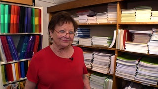 Inge Walter steht in ihrem Schreibwarengeschäft in Sinzheim vor Regalen mit Heften und Mappen. Sie trägt ein totes T-Shirt und eine Brille.