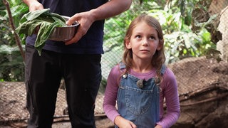 Die achtjährige Lena möchte Zoodirektorin werden. Sie steht in einem Gehege im Karlsruher Zoo und trägt eine Latzhose und ein rosa Langarmshirt.