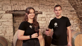 Mann und Frau stehen vor einem Weinfass