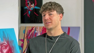 Künstler Fabian Utta vor einigen seiner Bilder