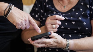 Ein Finger deutet auf das Handy einer älteren Frau