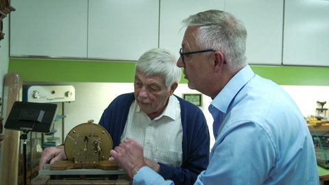 Zwei Männer arbeiten an einem Uhrwerk