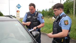 Zwei Polizeibeamte befragen eine Autofahrer auf einer Raststätte