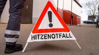 Notarzt stellt Warnschild mit Aufschrift: Hitzenotfall auf.