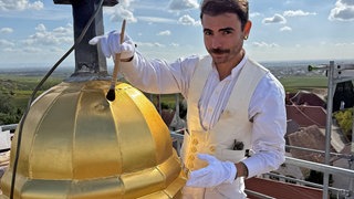 Malermeister Saymon Salviano vergoldet in luftiger Höhe die Kirchturmkugel in Dackenheim
