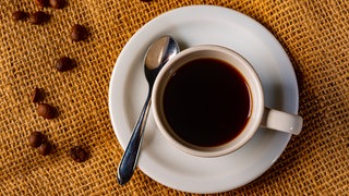 Tasse mit schwarzem Kaffee auf einem Tisch, dekoriert mit Kaffeebohnen