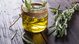 Kleines Glas befüllt mit Öl und Rosmarin. Rosmarin ist nicht nur beliebt als Gewürz, sondern ein bewährtes Naturheilmittel in der Medizin. Wertvolle Inhaltsstoffe wirken belebend, helfen bei Neurodermitis und niedrigem Blutdruck.