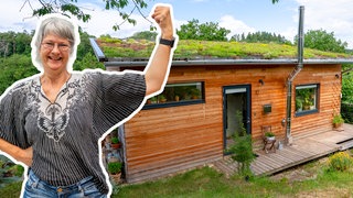 Nicole steht vor ihrem selbstgebauten Tiny House aus Holz im Grünen