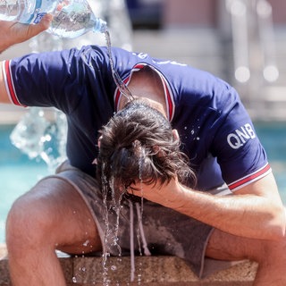Ein Mann gießt sich Wasser aus einer Flasche über den Kopf